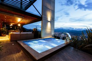 Piscina en terraza al anochecer, con cascada y vista a las luces de la ciudad y las montañas